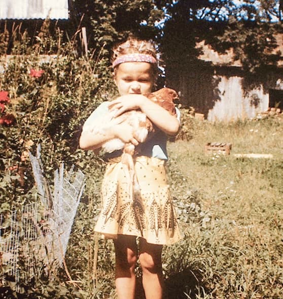 Artist Liene in age of 5 standing in garden and holding on hands hen